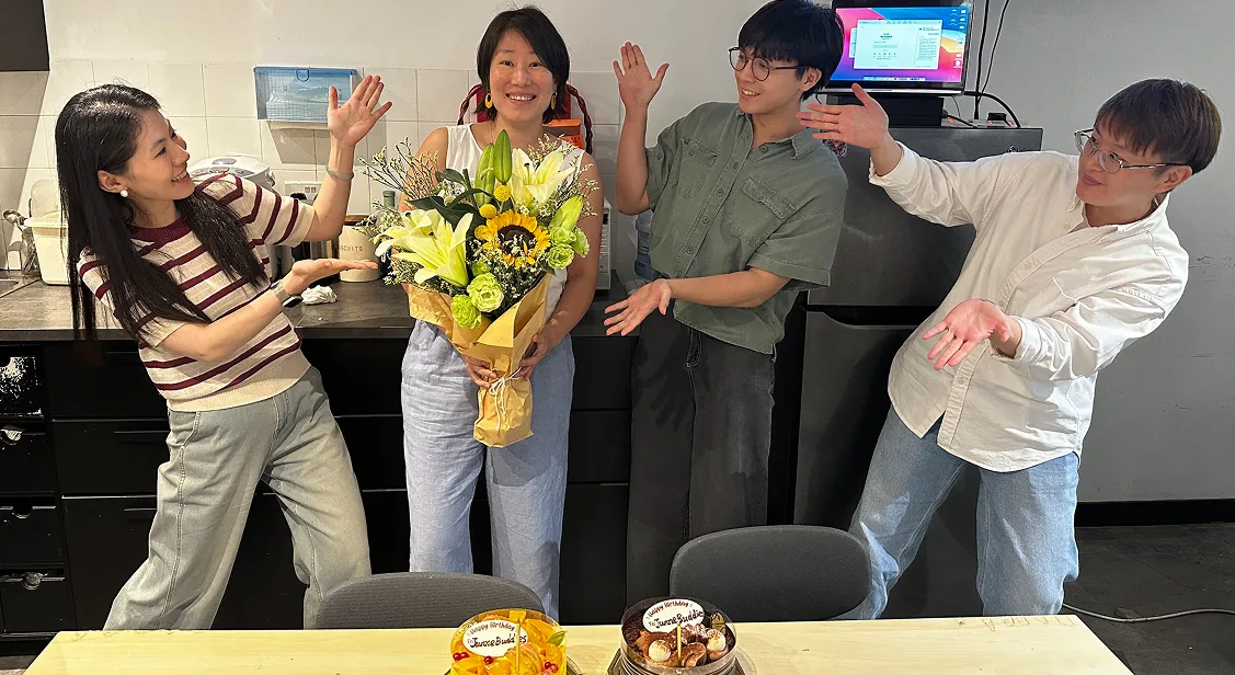 Teammates celebrating a birthday with flowers and cake in the office kitchen